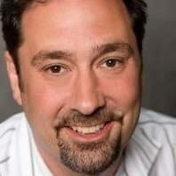 A smiling man with a beard and mustache wearing a white jacket is featured in our "About Us" section.