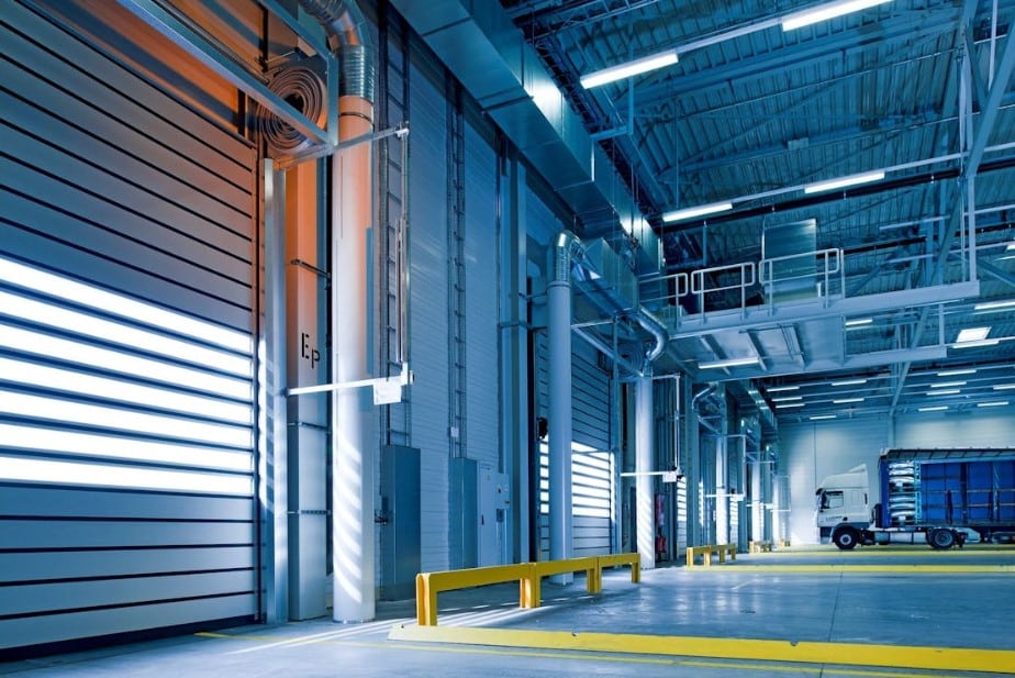 Interior of a modern cold storage warehouse with bright blue lights, featuring large shipping doors and a truck parked inside.