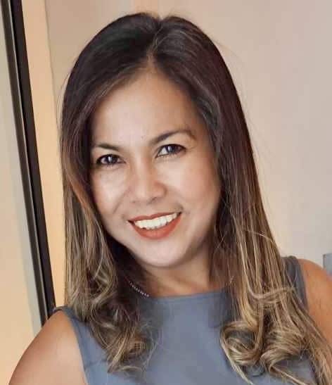 A woman with long, wavy hair smiles warmly, embodying the spirit of our company values in her gray sleeveless top—truly capturing the essence of "About Us.