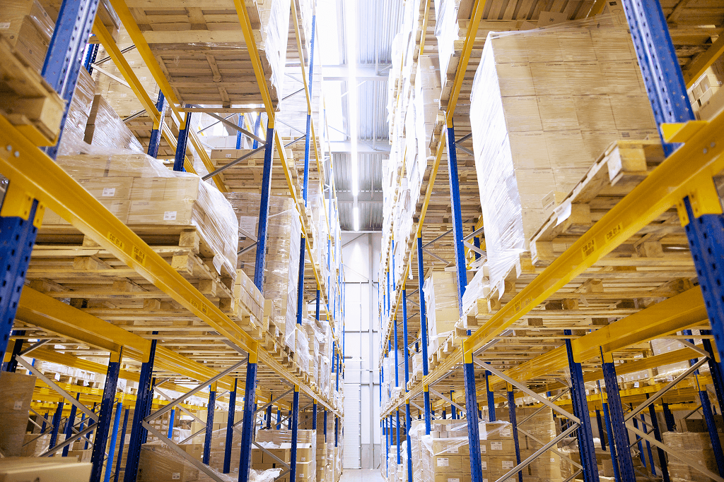 Chicago cold storage facility features a warehouse interior with tall blue and yellow shelves stacked with palletized boxes on both sides of a bright aisle.