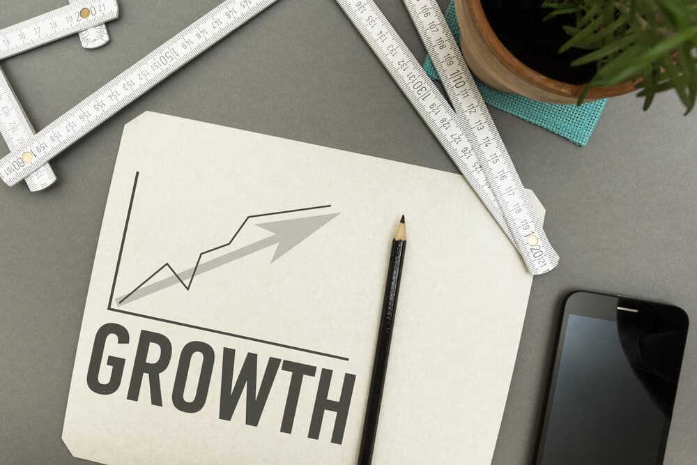 Paper with a chart showing upward growth, a pencil, folding rulers, a plant, and a smartphone arranged on a gray surface—perfect for planning your Shopify Ecommerce fulfillment strategy.