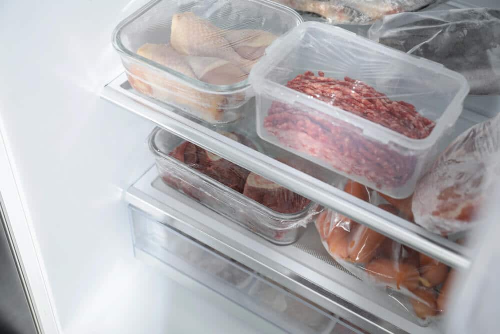 Plastic containers of raw meat and fish are stored on shelves inside a refrigerator, ensuring proper cold storage for seamless inventory sync with NetSuite ERP.