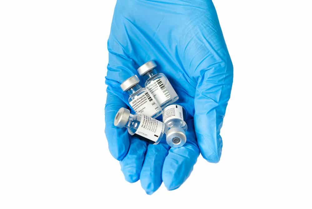 A gloved hand holds several small vaccine vials with labels against a white background, illustrating the precision essential for ERP for professional services logistics in service-based fulfillment operations.