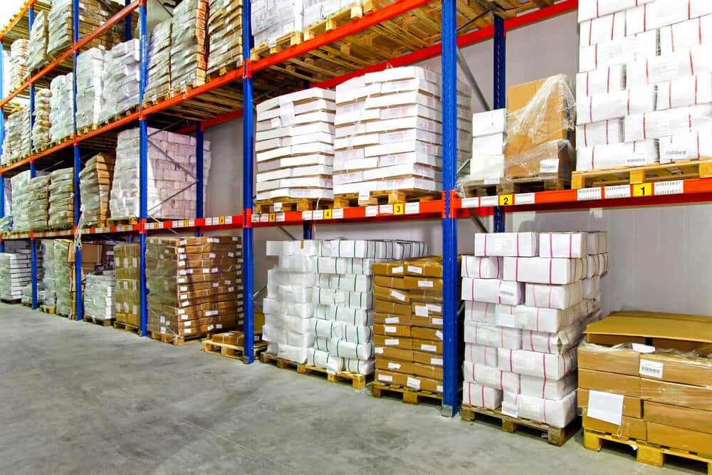 Warehouse shelves stocked with neatly stacked boxes and packages on wooden pallets along a concrete floor, optimized by the Salesforce Fulfillment Solution for efficient inventory management.