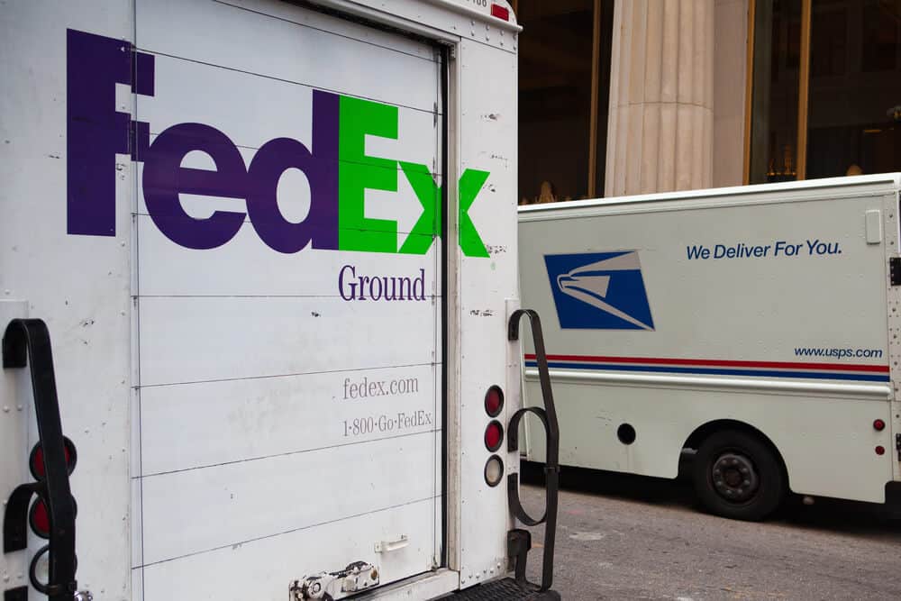 A FedEx Ground delivery truck is parked next to a USPS mail truck, highlighting the bustling city’s mix of carriers and USPS Fulfillment Solutions.