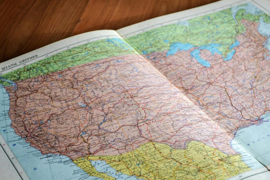 An open map book showing a detailed map of the United States, with state borders, cities, and geographic features visible on a wooden surface.
