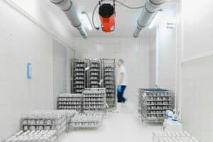 A person in protective clothing walks past racks filled with eggs in a clean, white industrial room—demonstrating the precision and standards essential for subscription box fulfillment.